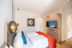 A modern hotel room with a bed, a TV, a wall-mounted artwork, and a wooden floor. - Beachhouse Bansin, App. 21 (Heringsdorf)