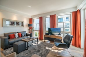 A modern living room with a sofa, ottoman, coffee table, and a TV on a stand. - Beachhouse Bansin, App. 21 (Heringsdorf)