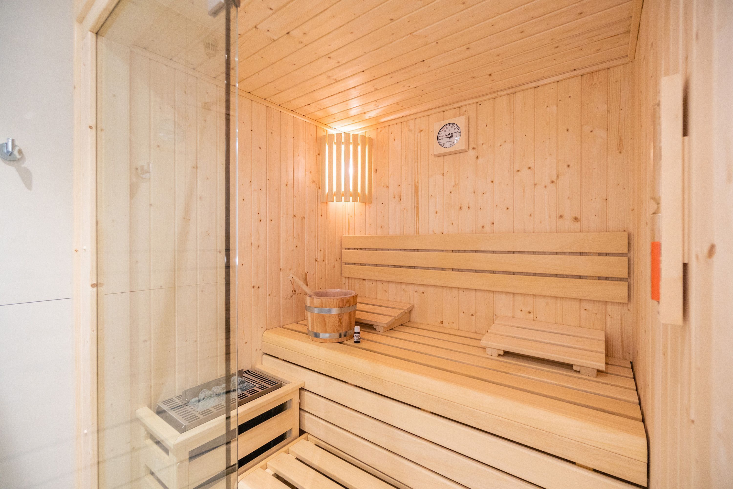 Eine Holzsauna mit Bänken, einem Holzeimer und einer an der Wand befestigten Uhr.