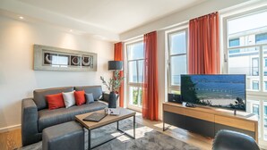 A modern living room with a sofa, a coffee table, a flat-screen TV, and large windows with curtains. - Beachhouse Bansin, App. 21 (Heringsdorf)