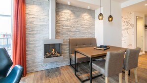 A modern living room with a stone wall, a fireplace, a dining table with chairs, and a view of the outside through a window with red curtains. - Beachhouse Bansin, App. 21 (Heringsdorf)