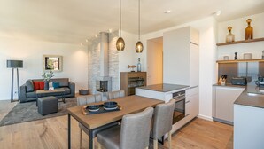A modern kitchen with a central island, dining area with a wooden table and chairs, and a cozy living space with a sofa and a fireplace. - Beachhouse Bansin, App. 19 (Heringsdorf)