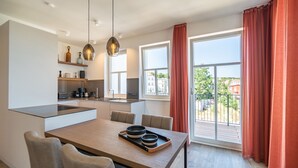 A modern kitchen with a central island, dining table with chairs, and a view of the outdoors through large windows. - Beachhouse Bansin, App. 19 (Heringsdorf)