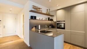 A modern kitchen with a central island, wooden shelves above, and a built-in oven. - Beachhouse Bansin, App. 18 (Heringsdorf)