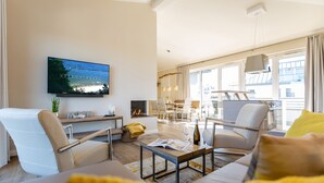 Een moderne woonkamer met een flatscreen televisie, comfortabele zithoek, een open haard en grote ramen met uitzicht.
