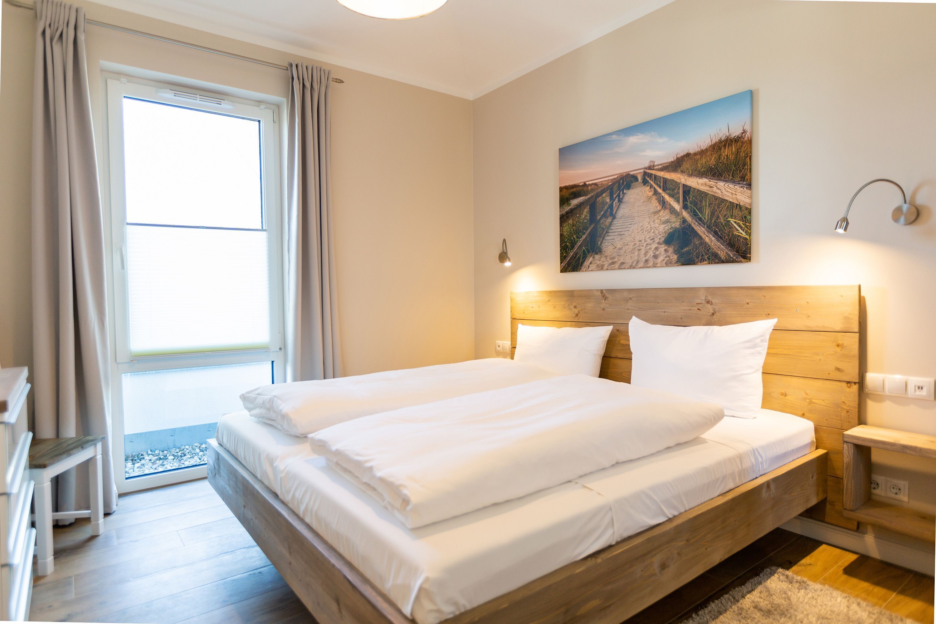 Ein Schlafzimmer mit einem großen Bett, einem hölzernen Kopfteil, einem Nachttisch, einer Wandlampe und einem Gemälde zum Strandthema.