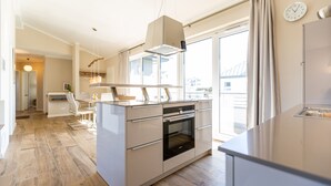 Een moderne keuken met een ingebouwde oven, een eethoek met een tafel en stoelen, en uitzicht op de stad door grote ramen.