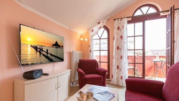 Een woonkamer met een televisie, een rode fauteuil, een witte kast en een tafel met een kom en tijdschrift.