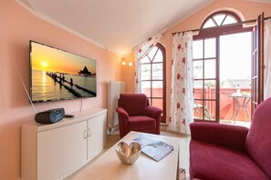 Uma sala de estar com televisão, uma poltrona vermelha, um armário branco e uma mesa com uma tigela e revista.