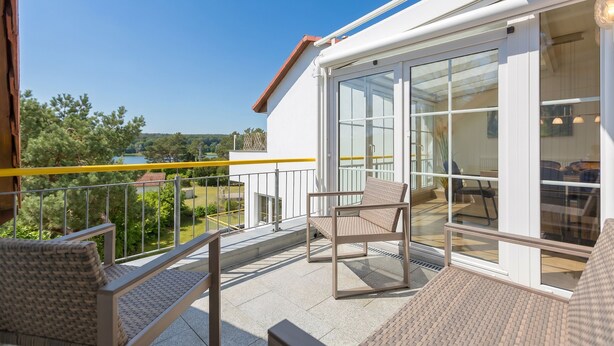 A balcony with two chairs, a table, and a glass door leading to an interior space. - Haus am Schloonsee, app. B7 (Heringsdorf)