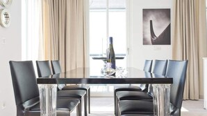 Una sala da pranzo moderna con tavolo in vetro, sedie in pelle nera e un'ampia finestra con tende.