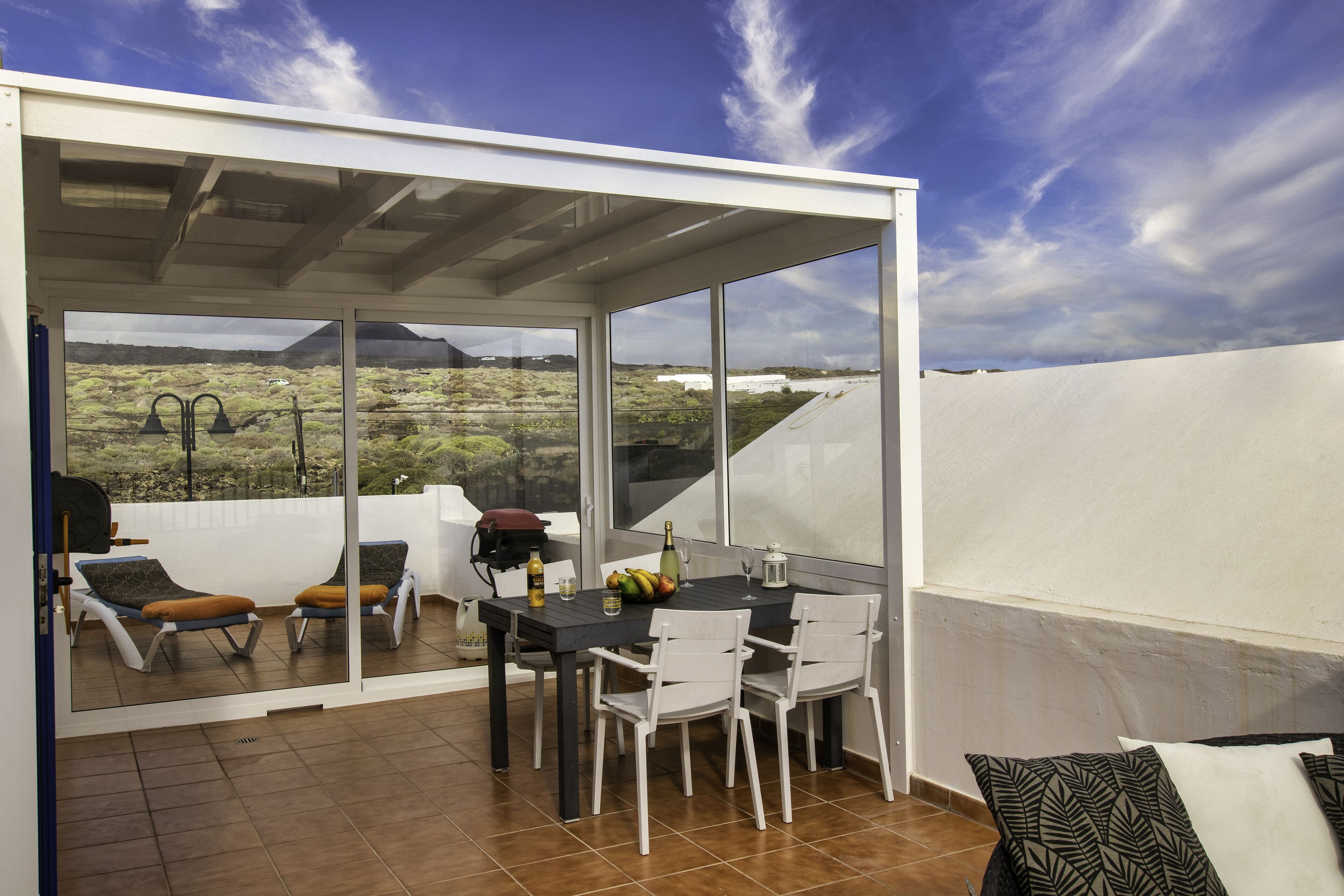 A covered patio with a table, chairs, and a view of a mountainous landscape.