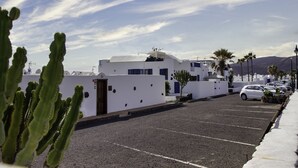 Un parking avec des bâtiments blancs, des voitures garées et un cactus au premier plan.