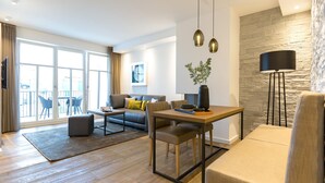 Ein modernes Wohnzimmer mit Sofa, Couchtisch und Esstisch. Es gibt ein großes Fenster mit Vorhängen, eine Steinwand und eine Stehlampe.