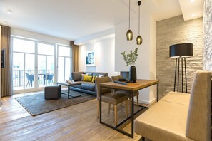 Un salón moderno con sofá, mesa de centro y mesa de comedor. Cuenta con un ventanal con cortinas, una pared de piedra y una lámpara de pie.