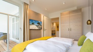 Ein modernes Hotelzimmer mit einem großen Bett, einem Gemälde mit Strandmotiv, einer Schiebetür zu einem Balkon und einem Holzschrank.
