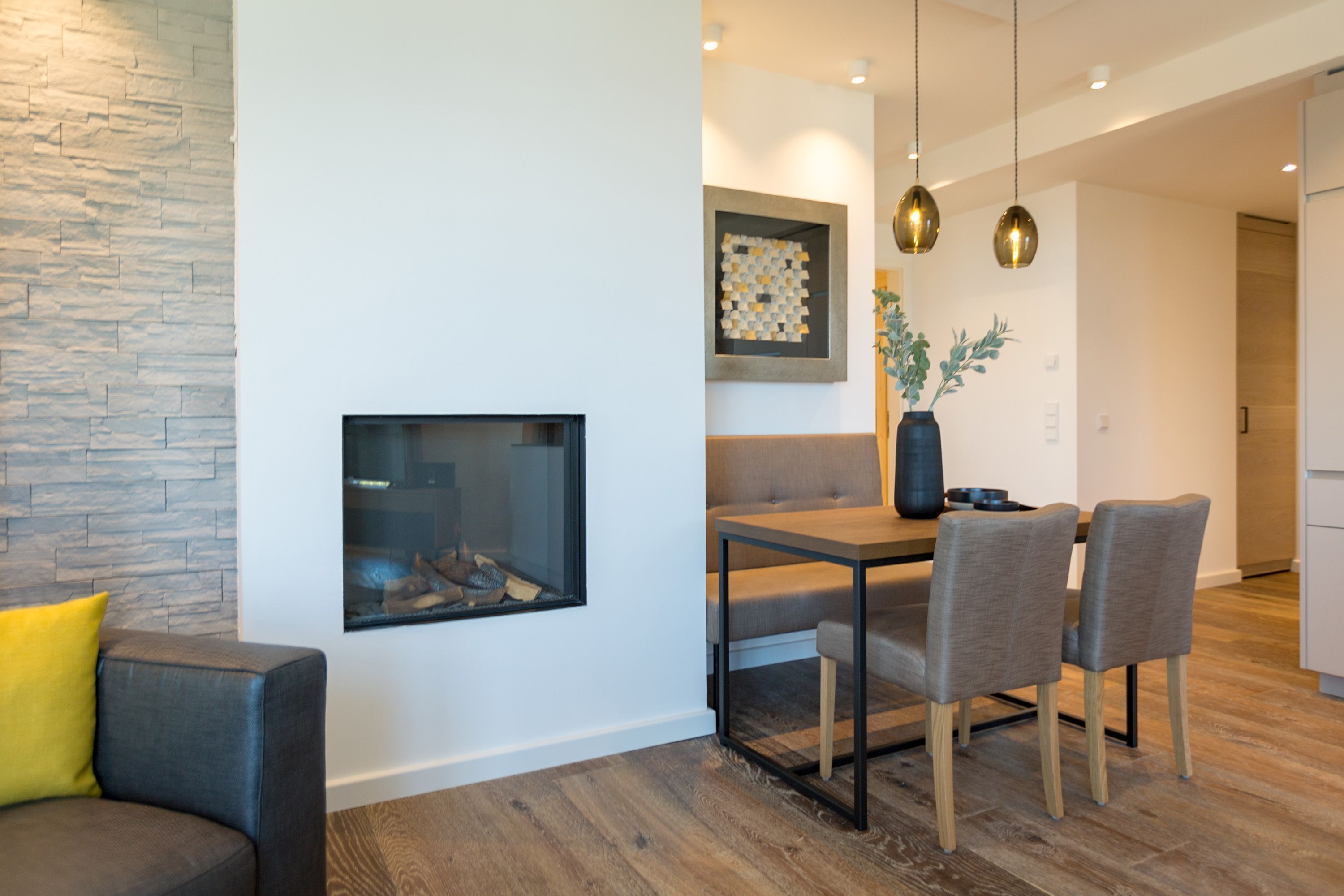 Una sala de estar moderna con chimenea, un comedor con mesa y sillas, y un sofá con un cojín amarillo.