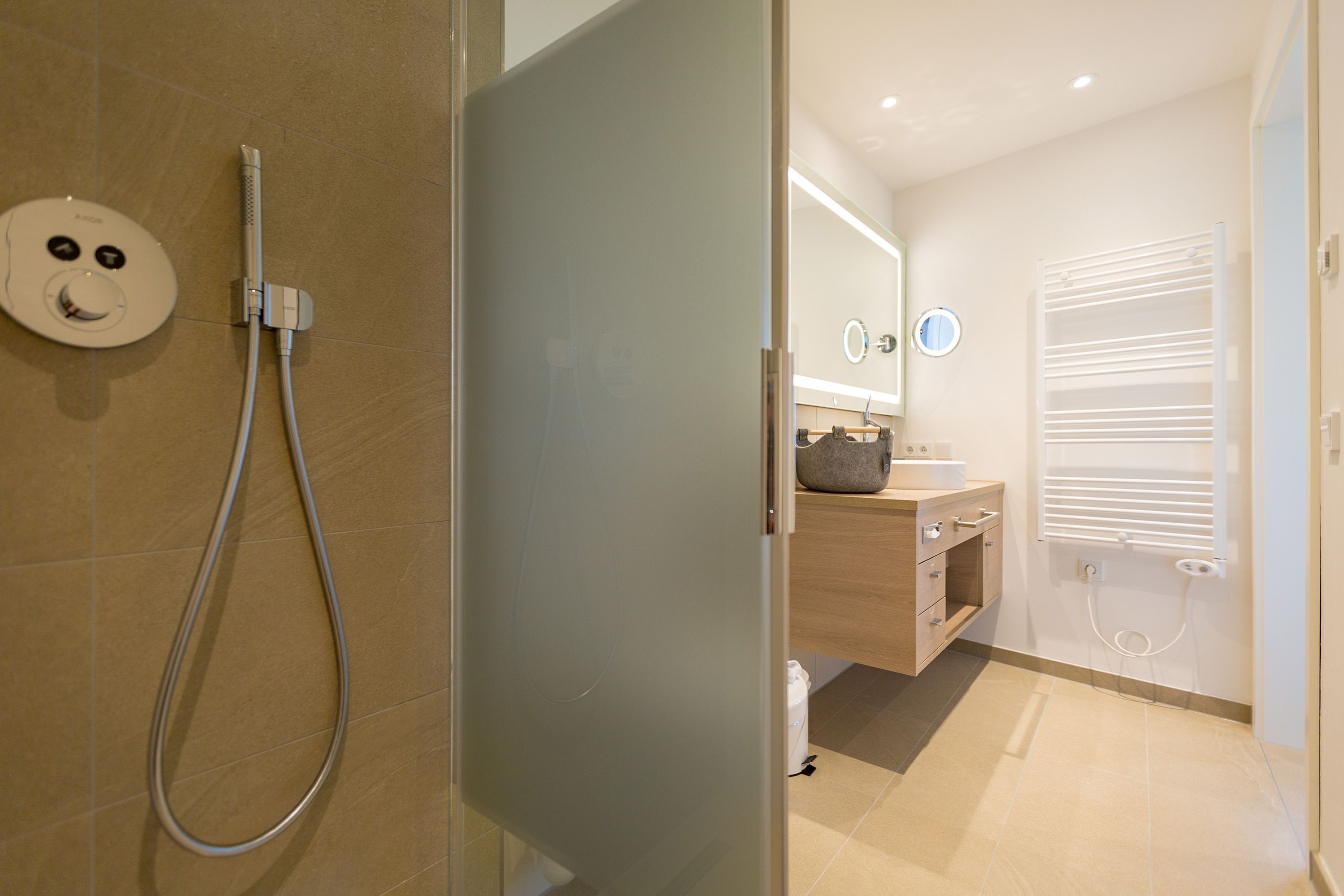 Ein modernes Badezimmer mit Duschkabine aus Glas, Toilette und Waschbecken mit Spiegel darüber.
