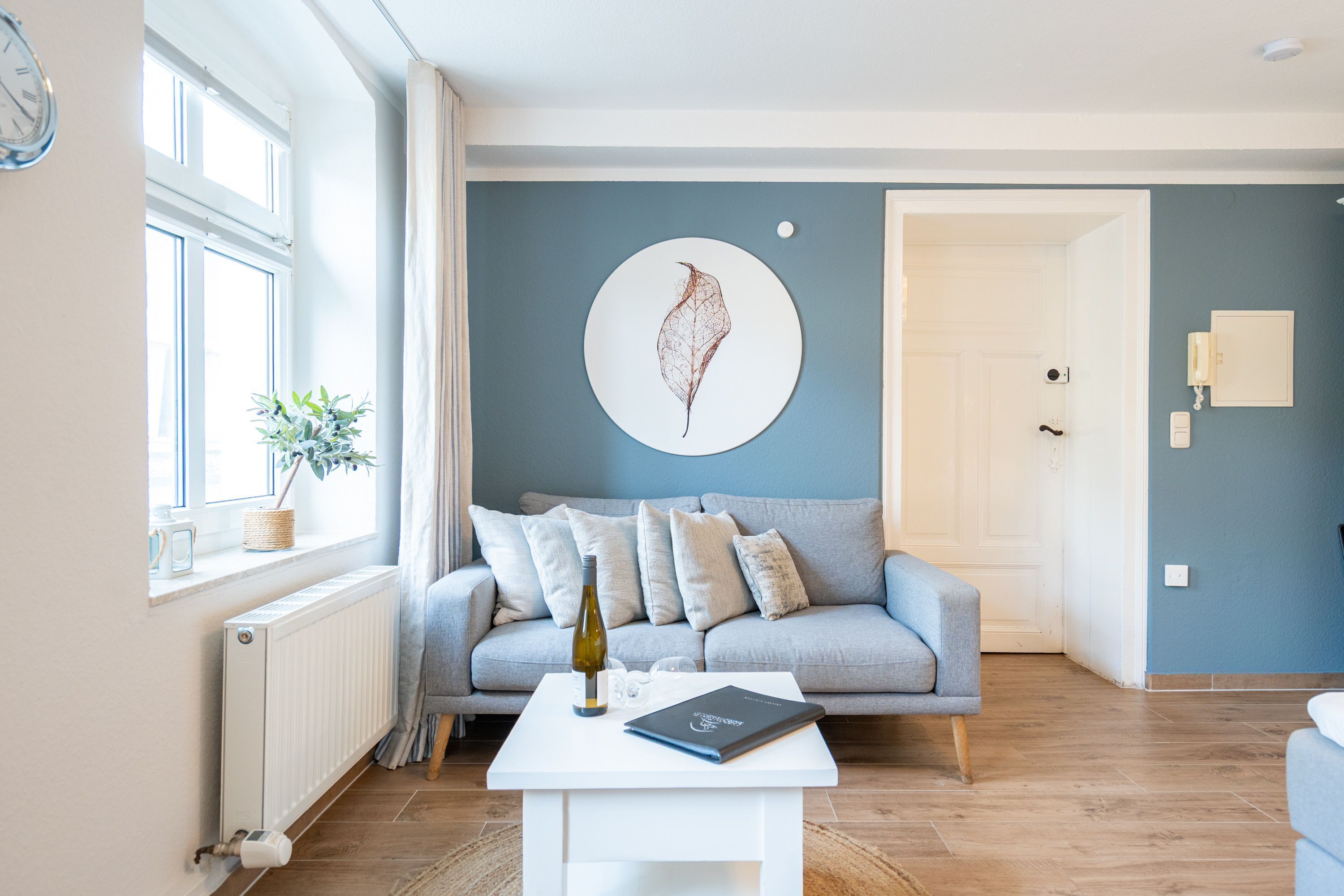 Ein modernes Wohnzimmer mit einem grauen Sofa, einem weißen Couchtisch und einem großen Fenster mit Vorhängen.