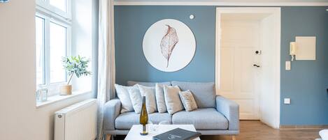 Ein modernes Wohnzimmer mit einem grauen Sofa, einem weißen Couchtisch und einem großen Fenster mit Vorhängen.