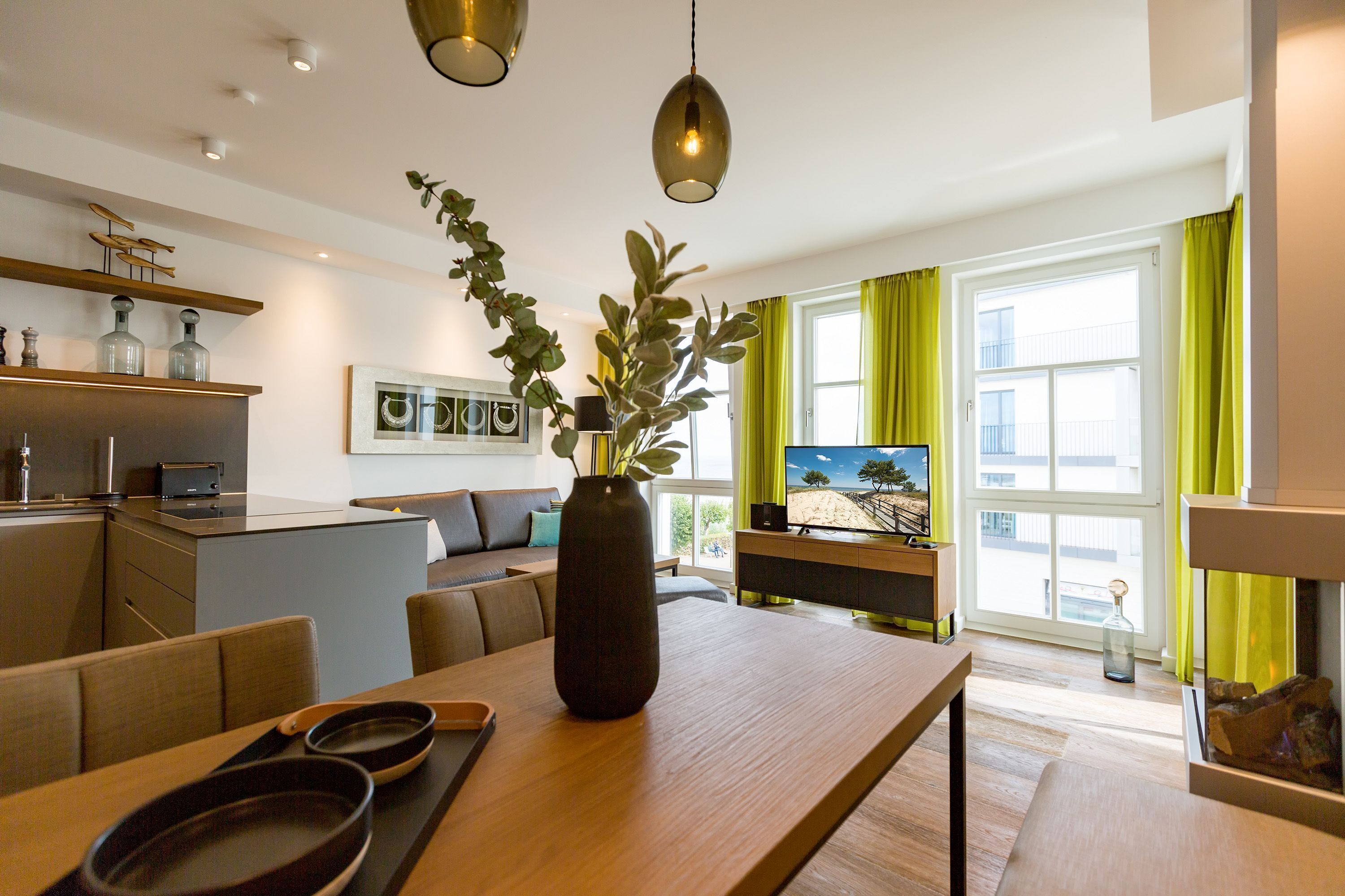 A modern kitchen with a dining area, a large window with curtains, and a view of the outside.