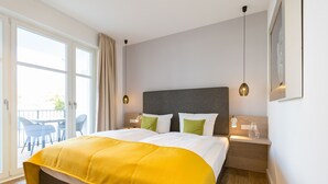 Une chambre avec un grand lit, une table de chevet, une lampe et une vue sur l’extérieur.