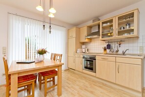 Une cuisine moderne avec des meubles en bois, un four encastré et un coin repas comprenant une table et des chaises.