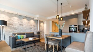 Una sala moderna con un sofá, una mesita de centro y una mesa de comedor. Se observa una zona de cocina con armarios y electrodomésticos.