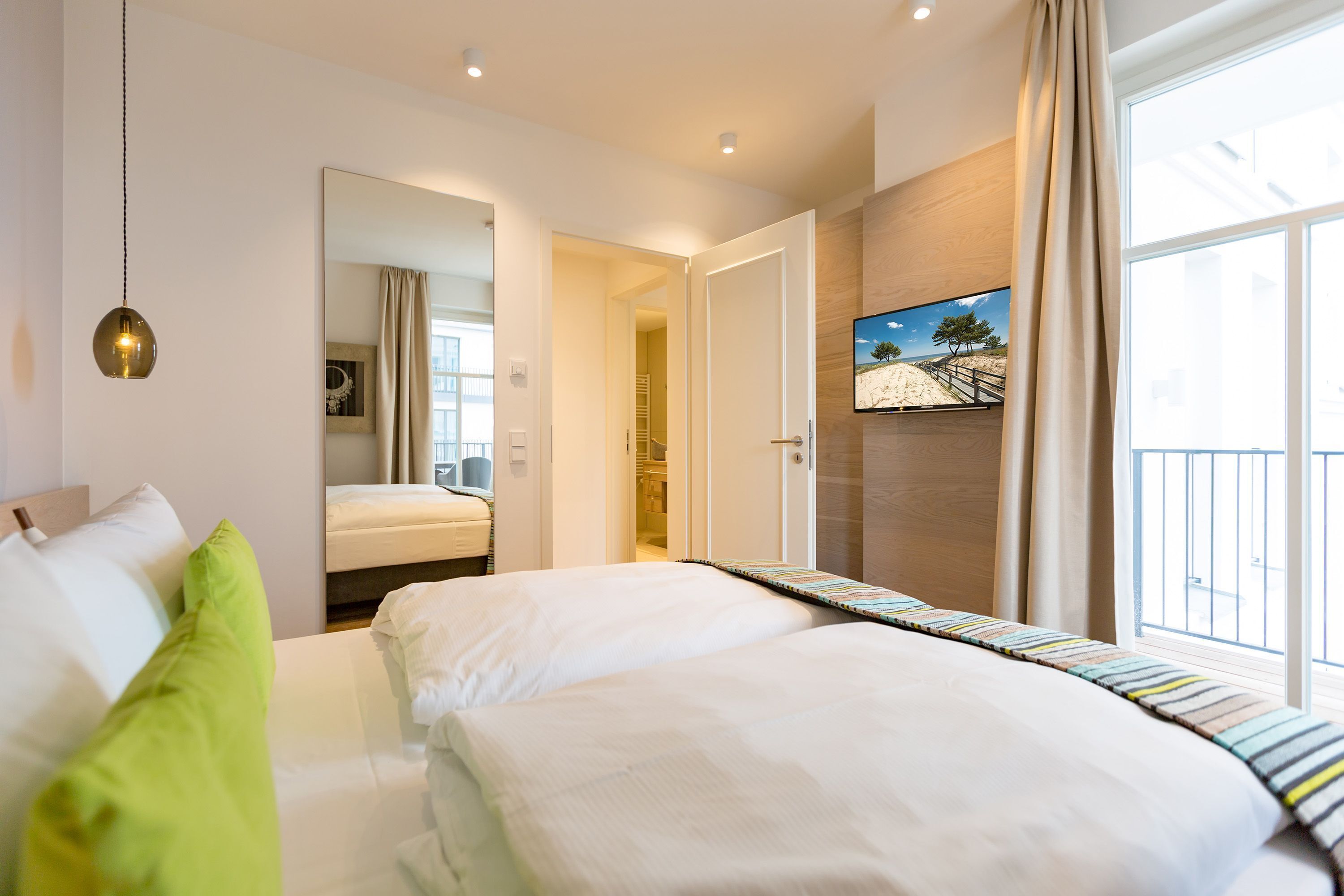 Habitación de hotel con una cama grande, un espejo, un televisor y un balcón con vistas a un paisaje desértico.
