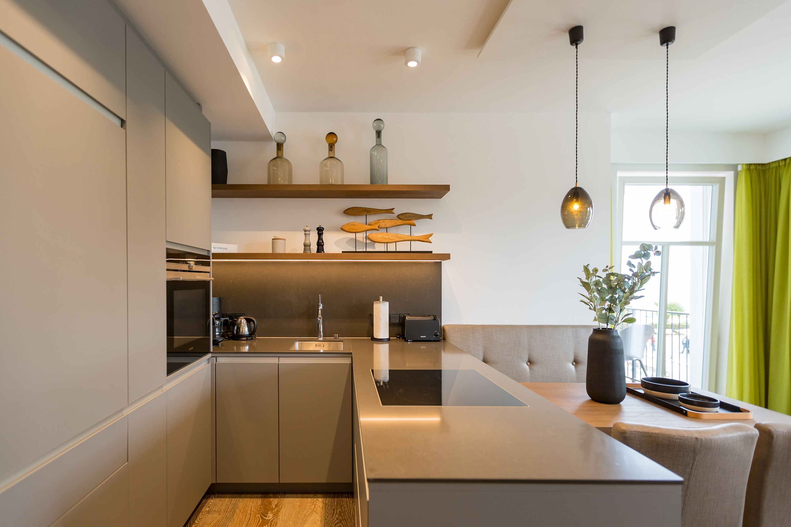 Moderni keittiö, jossa on integroidut kodinkoneet, ruokailutila ja näkymä ulos.