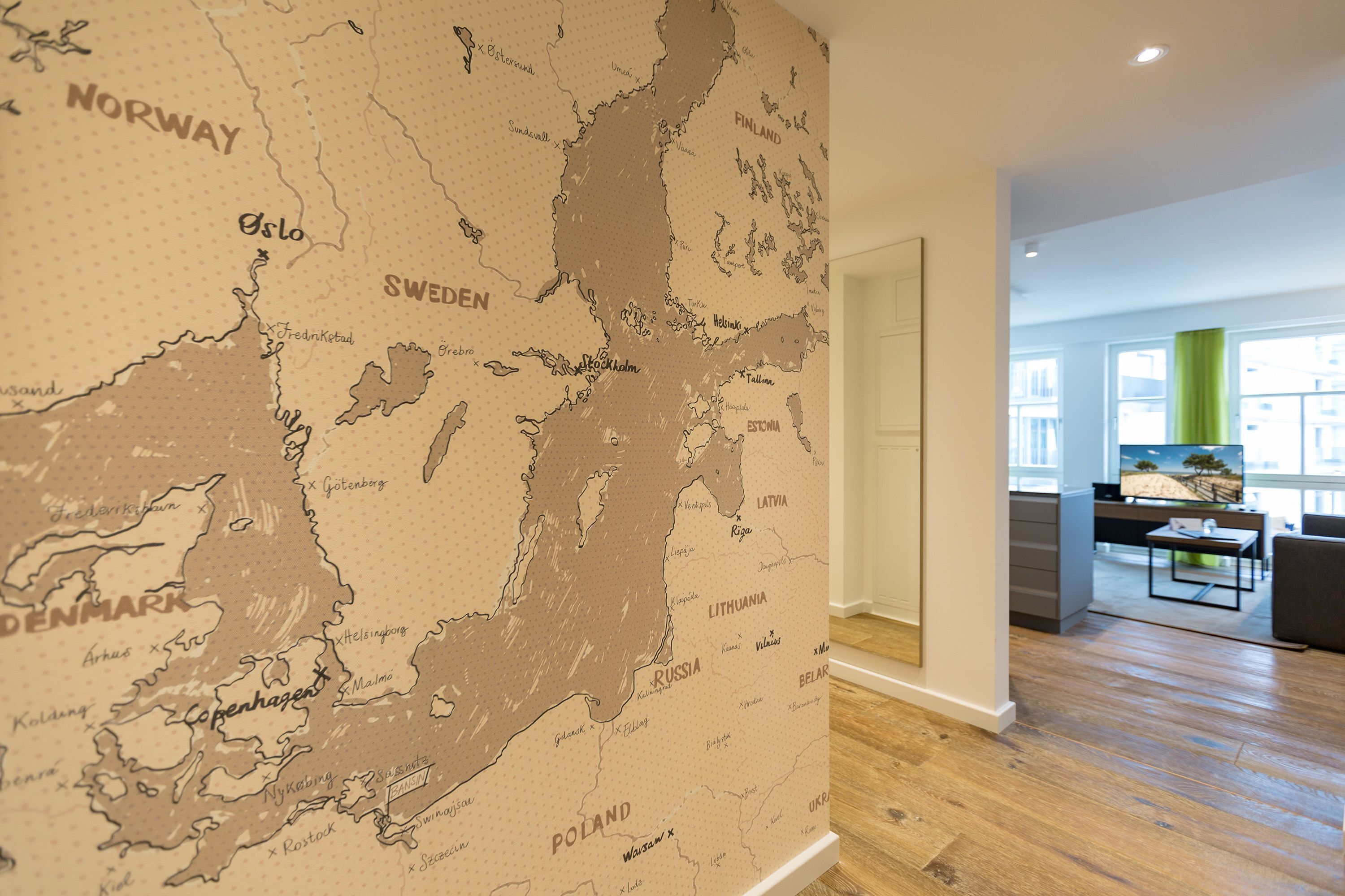 A map of Scandinavia on a wall, a wooden floor, and a modern kitchen area with a dining table.