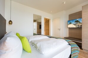 Une chambre à coucher moderne avec un grand lit, un téléviseur fixé au mur et un banc en bois.