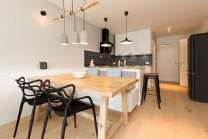 Cozinha moderna com mesa de madeira, cadeiras pretas, luminárias pendentes e uma geladeira preta.