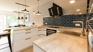 Una cucina moderna con una grande isola, illuminazione a sospensione e uno schienale in piastrelle blu.