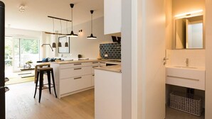 Una cucina moderna con mobili bianchi, un'isola centrale, luci a sospensione e vista sull'esterno.