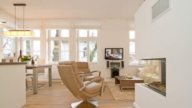 En moderne stue med en beige lædersofa, et spisebord og et fladskærms-tv monteret på væggen.