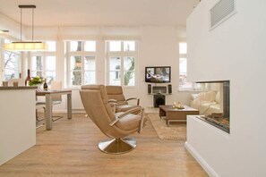 Un salon moderne avec un canapé en cuir beige, une table à manger et un téléviseur à écran plat fixé au mur.