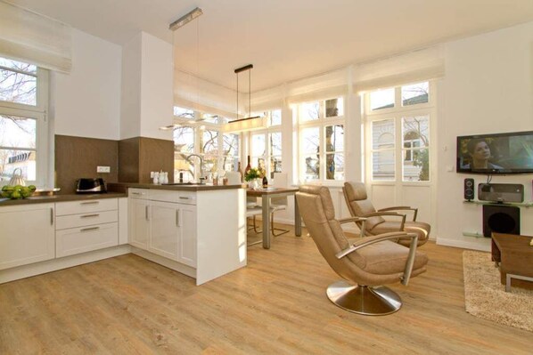 Une cuisine moderne avec des meubles blancs, un coin repas comprenant une table et des chaises, et une grande fenêtre laissant entrer la lumière naturelle.
