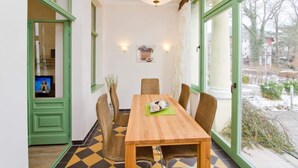 A dining area with a wooden table, wicker chairs, and a view of the outdoors through large windows. - Villa on the Baltic Sea beach, App. 5 (Heringsdorf)