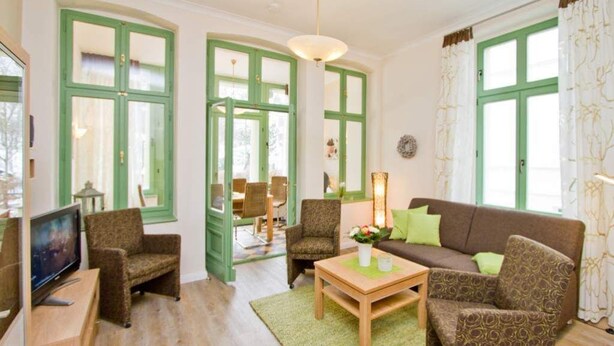 A living room with a brown sofa, two patterned armchairs, a wooden coffee table, and a television on a stand. - Villa on the Baltic Sea beach, App. 5 (Heringsdorf)