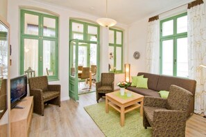 Een woonkamer met een bruine bank, twee fauteuils met een patroon, een houten salontafel en een televisie op een meubel.