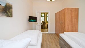 A room with two single beds, a wooden wardrobe, a television mounted on the wall, and a door leading to another room. - Villa on the Baltic Sea beach, App. 5 (Heringsdorf)