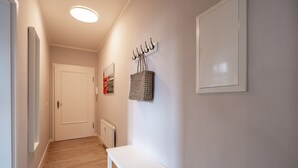 Un pasillo con una puerta blanca, un banco blanco y un panel con ganchos en la pared.