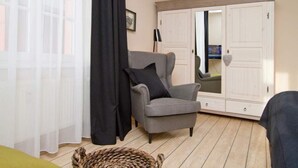 A room with a grey armchair, a black curtain, a woven basket, and a white wardrobe with a mirror.