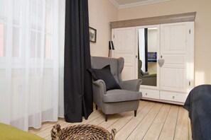 A room with a grey armchair, a black curtain, a woven basket, and a white wardrobe with a mirror.