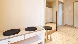 A room with a white vanity, two black circular objects on it, a small stool, and a wooden floor.