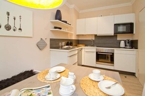 A modern kitchen with white cabinets, a microwave, and an oven. There is a dining table set with plates, cups, and a book.