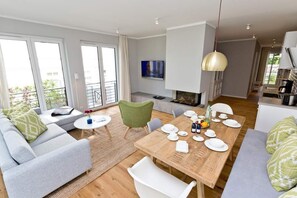 Un salon moderne avec un canapé, une table à manger pour quatre personnes, un fauteuil vert et un téléviseur fixé au mur.