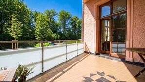 En balkon med udsigt til træer, flisegulv og gelænder.
