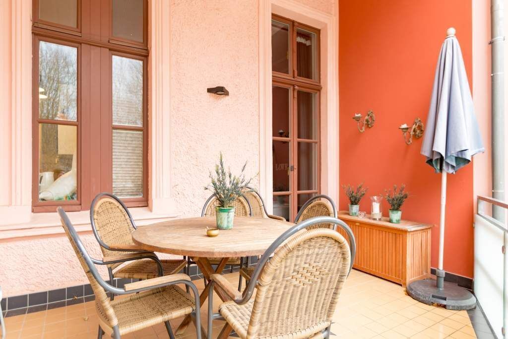 A dining area with a round table, wicker chairs, potted plants, and a wooden bench.